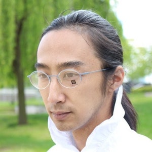 Puede incluir: Una persona con gafas redondas de montura transparente y una camisa blanca con cuello.