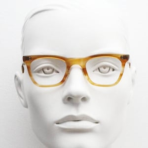 May include: A pair of eyeglasses with a light brown, tortoiseshell pattern frame. The glasses have a rectangular shape and are displayed on a white mannequin head. The frame has a subtle, speckled design.