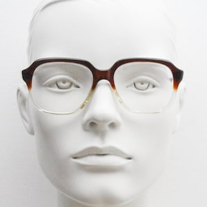 以下が含まれることがあります： 透明なレンズが付いたべっ甲柄の眼鏡。眼鏡は白いマネキンの頭に置かれています。