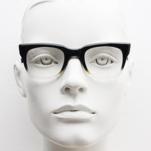 May include: Black and clear eyeglasses with a square frame design. The top of the frame is black, transitioning to clear at the bottom. The glasses are displayed on a white mannequin head.