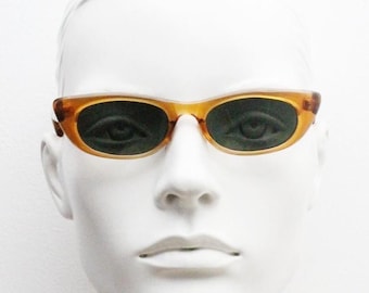 Könnte beinhalten: Ovale Sonnenbrille mit einem Schildpattrahmen und dunkelgrünen Gläsern. Die Sonnenbrille wird auf einem weißen Schaufensterpuppenkopf präsentiert. Der Rahmen hat ein subtiles, geschwungenes Design, und die Gläser sind tiefgrün.