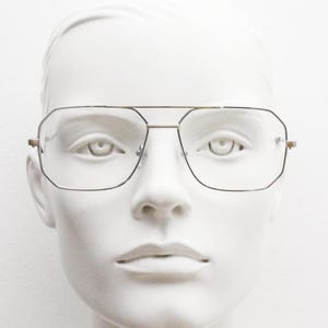 May include: A pair of gold-rimmed glasses with clear lenses. The glasses have a square shape with slightly rounded corners.