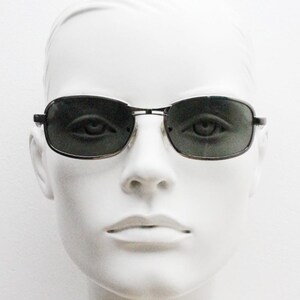 May include: A pair of black framed sunglasses with dark gray lenses. The sunglasses are on a white mannequin head.