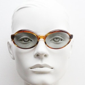 60s stylised oval vintage sunglasses. Mottled honey brown acetate frame with luxury grey glass lenses and thickened brows. Mod. Unworn NOS
