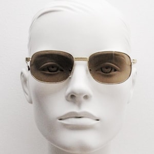 May include: A white mannequin head wearing gold-rimmed sunglasses with brown lenses.
