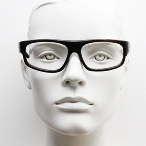 Puede incluir: Una cabeza de maniquí blanca con gafas rectangulares negras con lentes transparentes.
