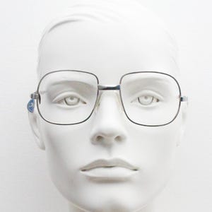 May include: Silver-framed square eyeglasses with clear lenses on a white mannequin head.
