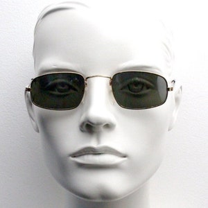 May include: A white mannequin head wearing gold-rimmed square sunglasses with dark green lenses.