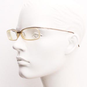 Könnte beinhalten: Rechteckige Brille mit hellbraunem Rahmen und Bügeln. Die Gläser sind hellgelb. Die Brille wird auf einem weißen Schaufensterpuppenkopf präsentiert.