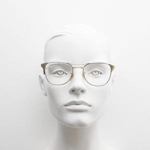 Puede incluir: Una cabeza de maniqu&iacute; blanca con gafas de montura dorada y lentes transparentes.