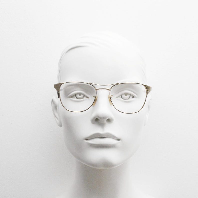 Puede incluir: Una cabeza de maniqu&iacute; blanca con gafas de montura dorada y lentes transparentes.