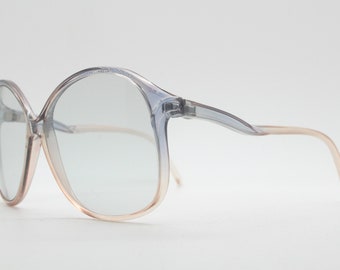 May include: A pair of clear plastic spectacles with a light pink tint on the edges. The glasses have a rounded, oversized frame.