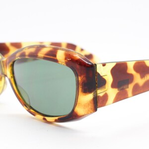Puede incluir: Gafas de sol de carey con lentes verdes. Las gafas tienen una forma redondeada y ovalada.