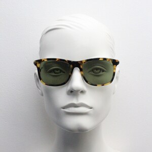 May include: A mannequin wearing tortoiseshell sunglasses with green lenses.