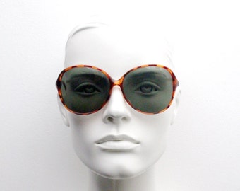 May include: A mannequin wearing tortoise shell sunglasses with brown frames and dark green lenses.