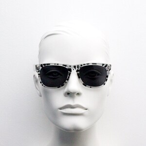 May include: A white mannequin head wearing black and white patterned sunglasses with black lenses.