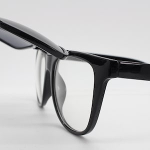 May include: Black plastic framed glasses with clear lenses and a flip-down sunglass shield.