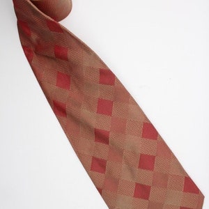 Może przedstawiać: Czerwono-brązowy krawat z jedwabiu w kratę. Krawat ma wzór w kratę z kwadratami o różnych rozmiarach.