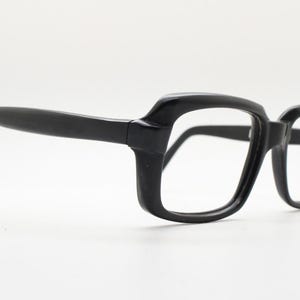 May include: Black plastic framed eyeglasses with a rectangular shape. The frames have a slight curve to them.