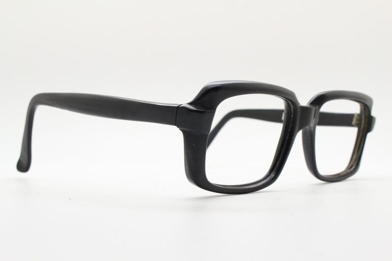 May include: Black plastic framed eyeglasses with a rectangular shape. The frames have a slight curve to them.