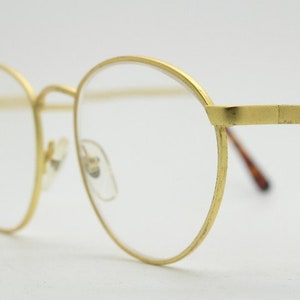 May include: Gold-tone round eyeglasses with clear lenses.