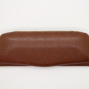 May include: A brown, rectangular eyeglasses case with a textured surface. The case is closed and has a slightly curved top and bottom. The edges are a lighter shade of brown.