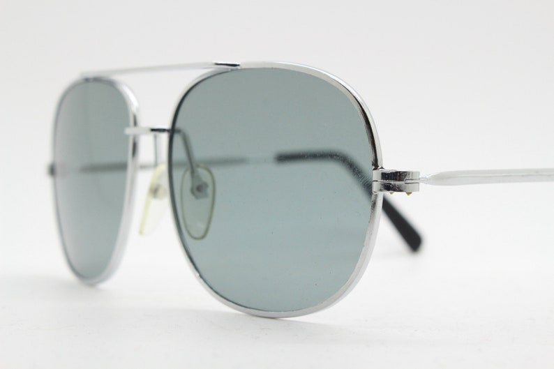 May include: Silver aviator sunglasses with gray lenses. The sunglasses have a metal frame and are in focus.