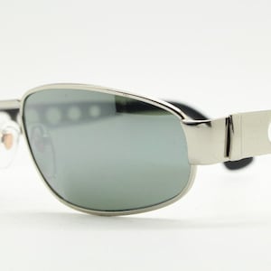 May include: Silver aviator sunglasses with a silver frame and gray lenses. The frame has a row of small holes on the side.