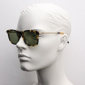 May include: Tortoiseshell sunglasses with green lenses and gold accents. The sunglasses are on a white mannequin head.