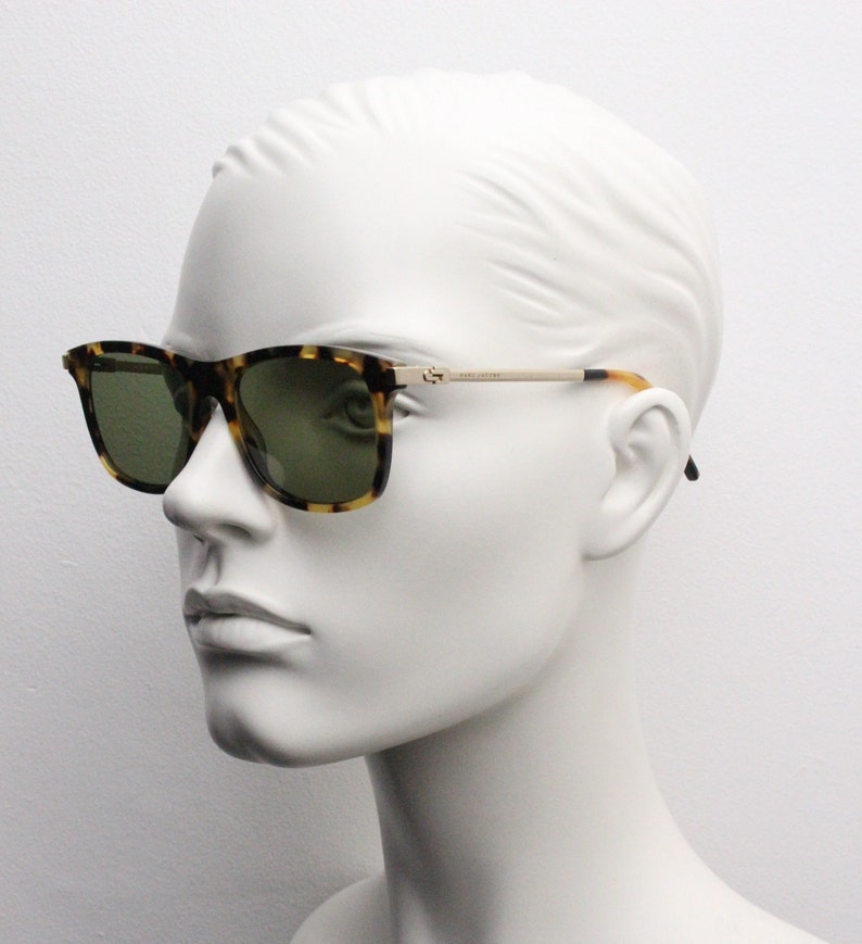 May include: Tortoiseshell sunglasses with green lenses and gold accents. The sunglasses are on a white mannequin head.