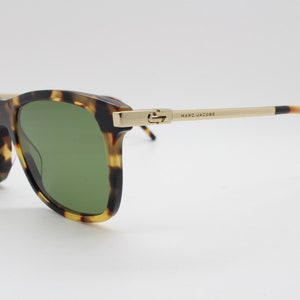 May include: Tortoiseshell sunglasses with green lenses and gold accents. The arms of the sunglasses are made of metal and have the text "MARC JACOBS" printed on them.