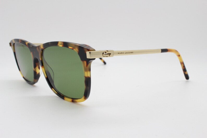 May include: Tortoiseshell sunglasses with green lenses and gold accents. The arms of the sunglasses are made of metal and have the text "MARC JACOBS" printed on them.
