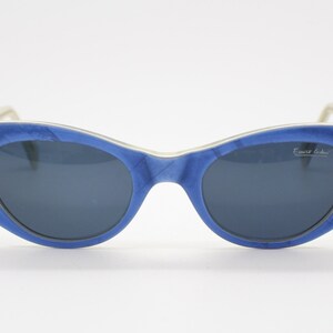 Op de afbeelding: Blauwe cat-eye zonnebril met gouden hart accenten en de tekst "Ernest Legrain" op de rechter lens.