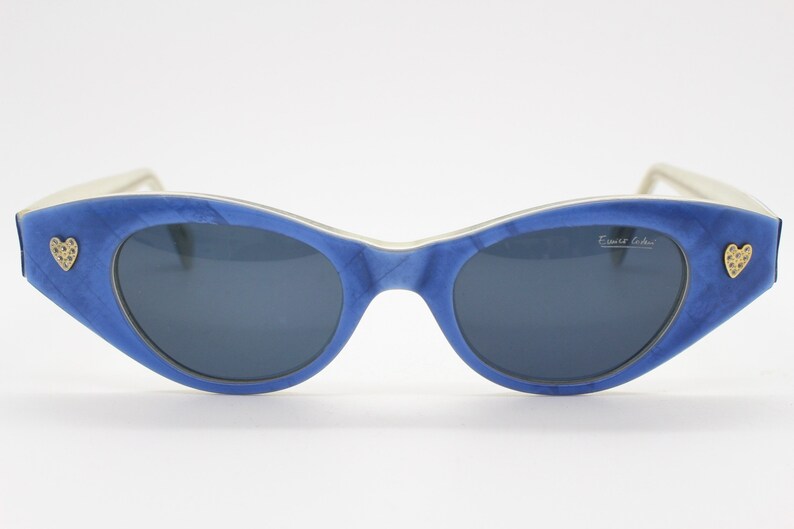 Op de afbeelding: Blauwe cat-eye zonnebril met gouden hart accenten en de tekst "Ernest Legrain" op de rechter lens.