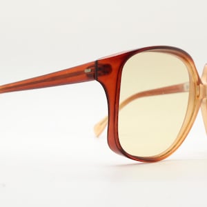 Op de afbeelding: Vintage oversized zonnebril met een bruin verloop montuur en geel getinte glazen. De monturen hebben een vierkante vorm met een licht cat-eye design. De pootjes zijn een lichtere bruintint.