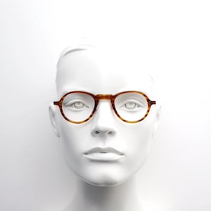 May include: Round eyeglasses with a tortoise shell pattern. The frames are a warm brown color and have a classic, vintage design. The glasses are displayed on a white mannequin head.