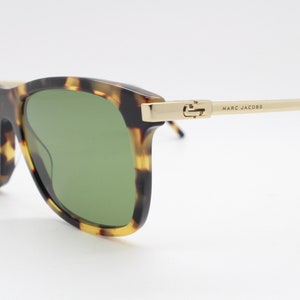 May include: Tortoiseshell sunglasses with green lenses and gold accents. The sunglasses have the brand name "MARC JACOBS" printed on the side.