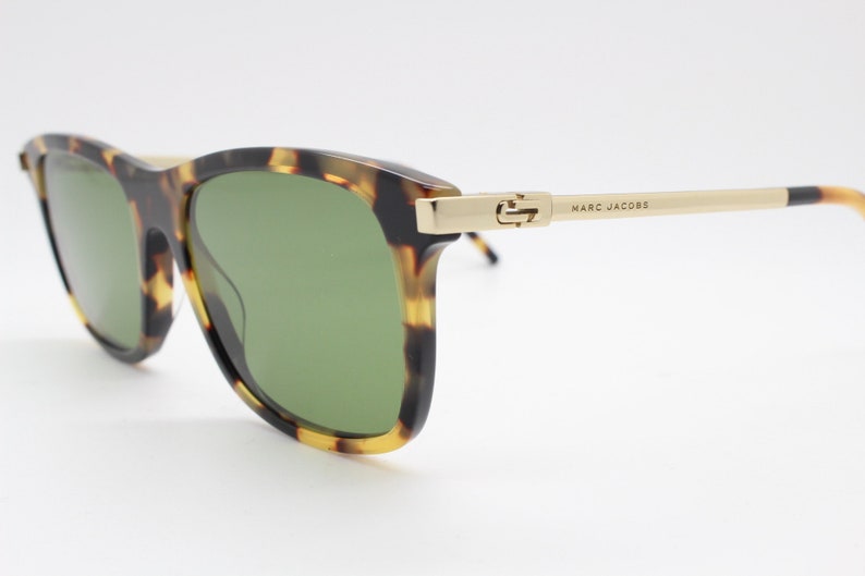 May include: Tortoiseshell sunglasses with green lenses and gold accents. The sunglasses have the brand name "MARC JACOBS" printed on the side.