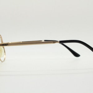 Puede incluir: Gafas de metal doradas con patillas de pl&aacute;stico negro. El nombre de la marca "FAUX" est&aacute; impreso en la montura.