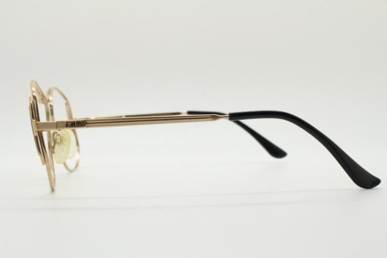 Puede incluir: Gafas de metal doradas con patillas de pl&aacute;stico negro. El nombre de la marca "FAUX" est&aacute; impreso en la montura.