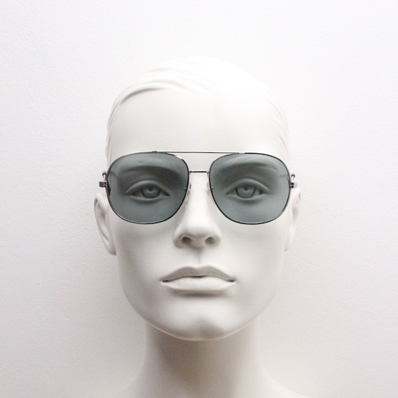 May include: A mannequin wearing silver aviator sunglasses with gray lenses.