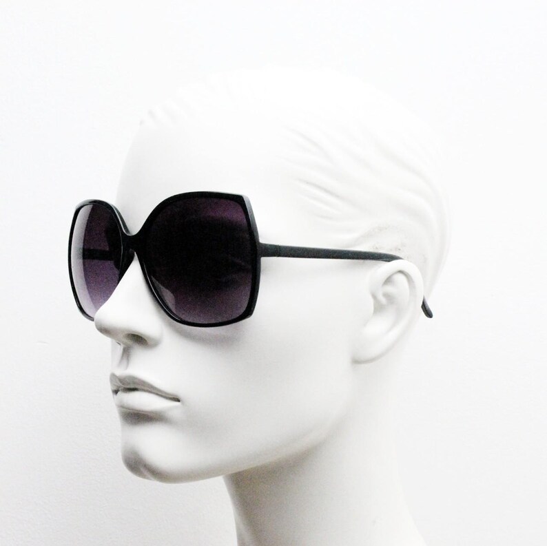 Puede incluir: Gafas de sol negras de gran tama&ntilde;o con montura geom&eacute;trica y lentes oscuras. Las gafas de sol est&aacute;n en una cabeza de maniqu&iacute; blanca.