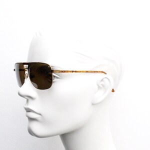 May include: A pair of gold-tone aviator sunglasses with brown lenses. The sunglasses are on a white mannequin head.