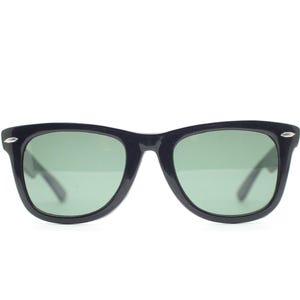 Puede incluir: Gafas de sol negras con lentes verdes. Las monturas son de color oscuro y s&oacute;lido, con una forma rectangular cl&aacute;sica. Peque&ntilde;os detalles plateados son visibles en las esquinas exteriores de las monturas. Las lentes son de color verde claro.