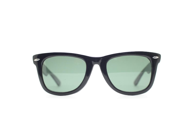 Puede incluir: Gafas de sol negras con lentes verdes. Las monturas son de color oscuro y s&oacute;lido, con una forma rectangular cl&aacute;sica. Peque&ntilde;os detalles plateados son visibles en las esquinas exteriores de las monturas. Las lentes son de color verde claro.