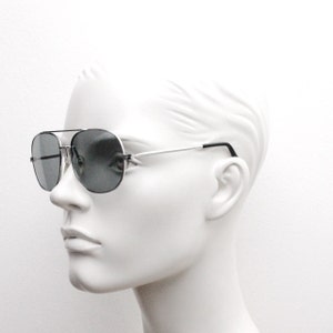 May include: Silver aviator sunglasses with dark gray lenses. The sunglasses are on a white mannequin head.