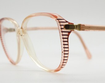 May include: A pair of pink plastic eyeglasses with a brown striped detail on the side of the frames.