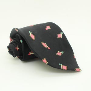 May include: A rolled black tie featuring a repeating pattern of pink diamond shapes and small green accents. The tie is made of a smooth fabric, suitable for formal or business wear.