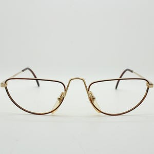 May include: Gold-toned eyeglasses with a half-rim design. The frames have a thin, delicate appearance with a brown accent along the bottom rim. The lenses are clear, and the nose bridge is a matching gold color.