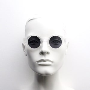 May include: Clear plastic framed round sunglasses with black lenses.